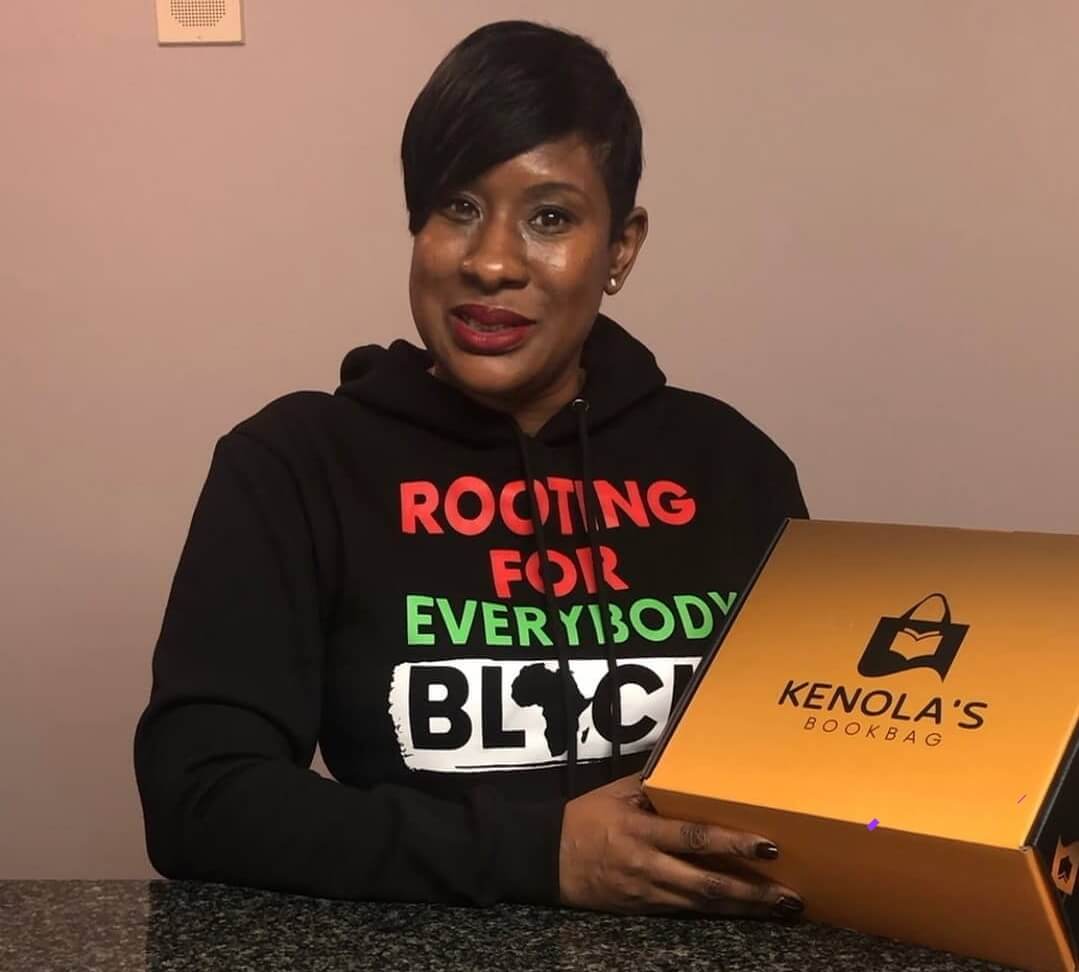 Black woman wearing osoasabrand sweatshirt and holding a Kenola's Bookbag fun subscription box.