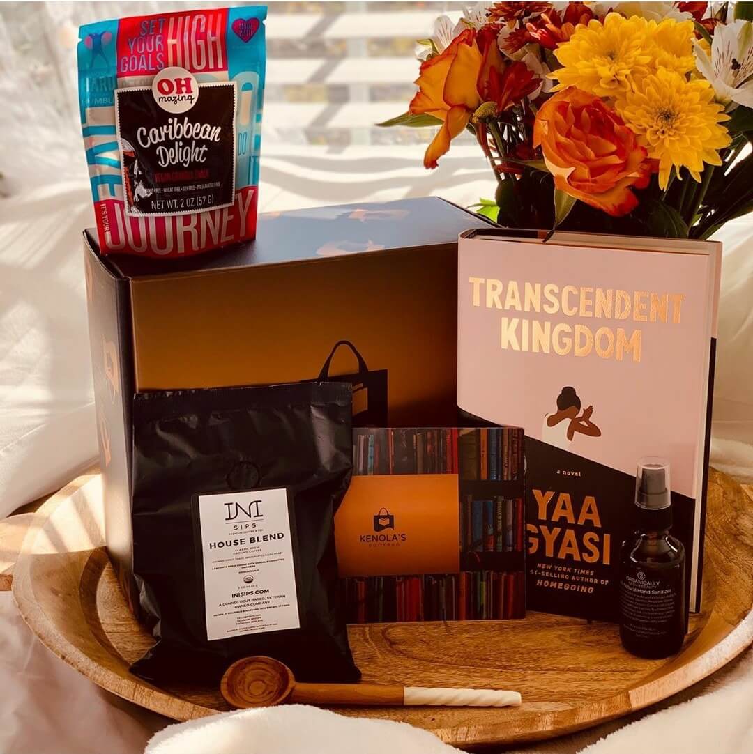A Kenola's curated subscription box surrounded by a book written by a Black author, a Kenyan wooden coffee spoon with ivory handle, a bag of granola,  bag of ground coffee, hand sanitizer and a bouquet of flowers.  All from Black owned businesses. 