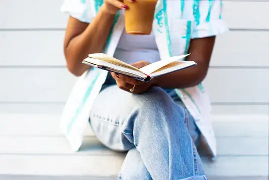 Black woman reading a book and drinking coffee.